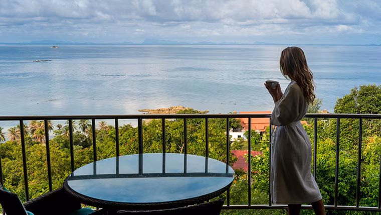 Woman in a robe with coffee on a balcony overlooking the sea in Phuket