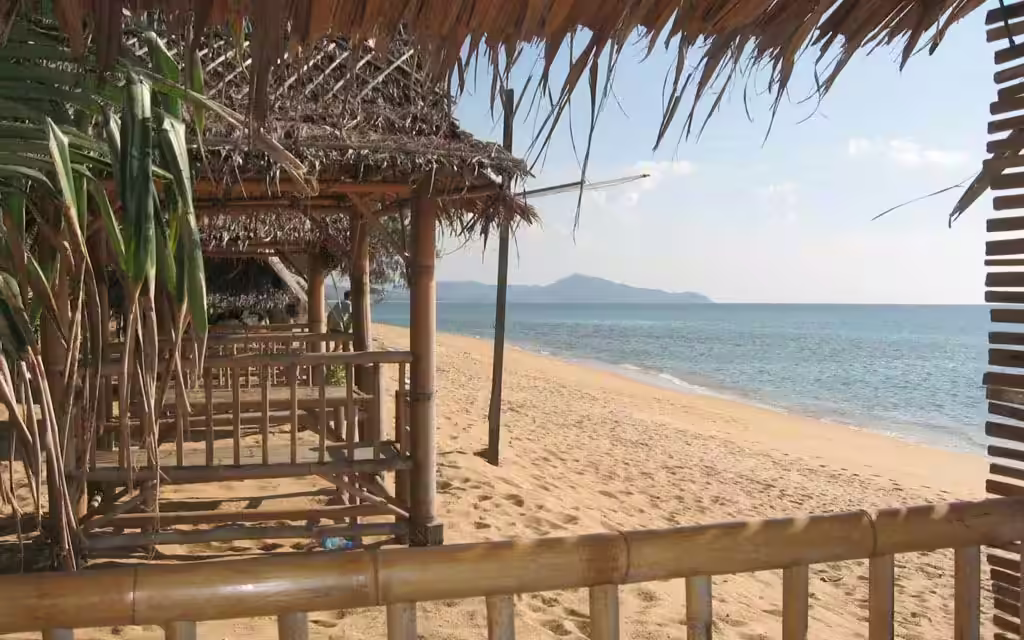 A thatched beachfront bar looking out over a quiet Phuket beach to the sea and an island